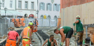 Mehrere Bauarbeiter arbeiten am Gleisbett einer großen Baustelle