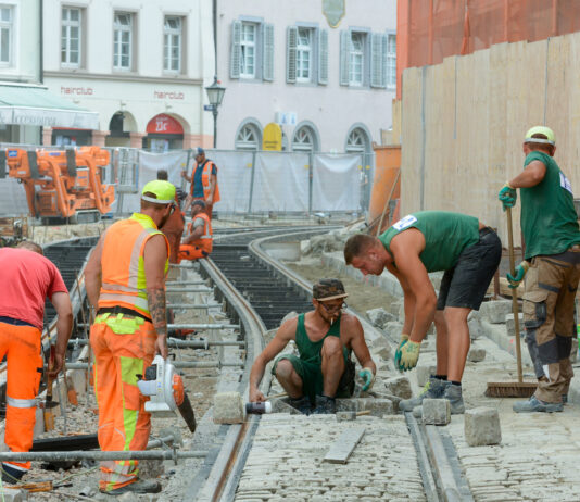 Mehrere Bauarbeiter arbeiten am Gleisbett einer großen Baustelle
