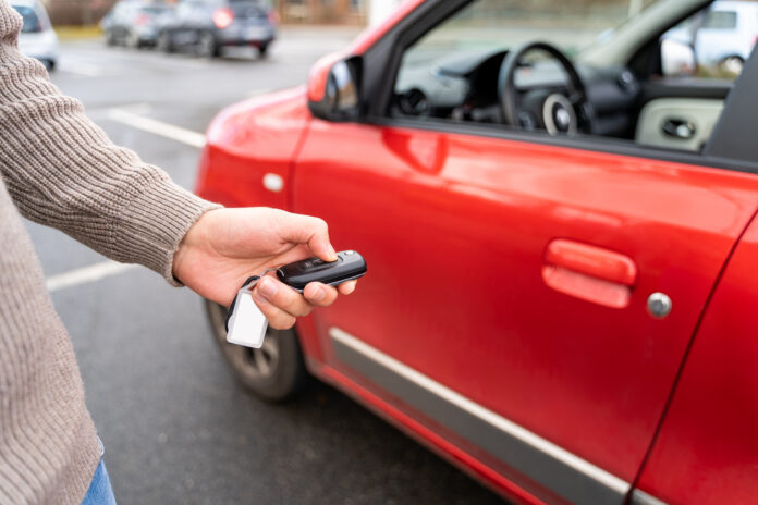 Männliche Hand hält elektronische Fernbedienung Druckknopf in der Nähe von der Autoscheibe eines roten Mietwagens