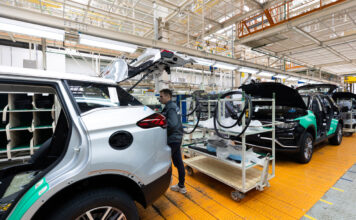 E-Auto-Produktion in einer Fabrik - ein Mitarbeiter schraubt gerade an der Rückseite im Bereich des Kofferraums an einem E-Auto oder an einem elektronischen Fahrzeug.