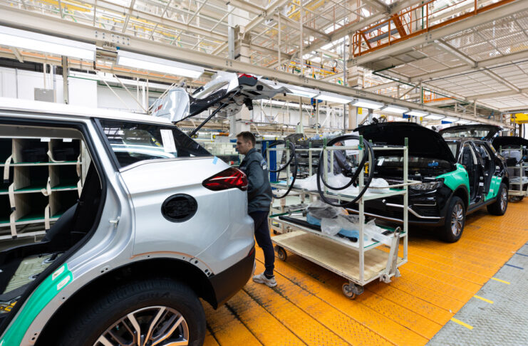 E-Auto-Produktion in einer Fabrik - ein Mitarbeiter schraubt gerade an der Rückseite im Bereich des Kofferraums an einem E-Auto oder an einem elektronischen Fahrzeug.