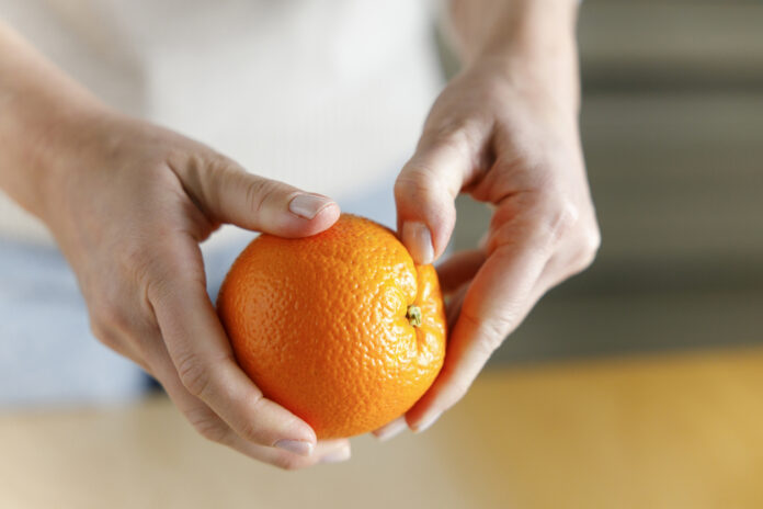 Frau hält eine Orange mit Orangenschale in den Händen