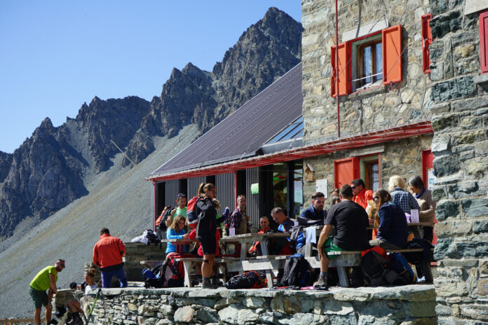 Zahlreiche Urlauber sind auf der Terrasse einer gastronomischen Einrichtung inmitten der Berge