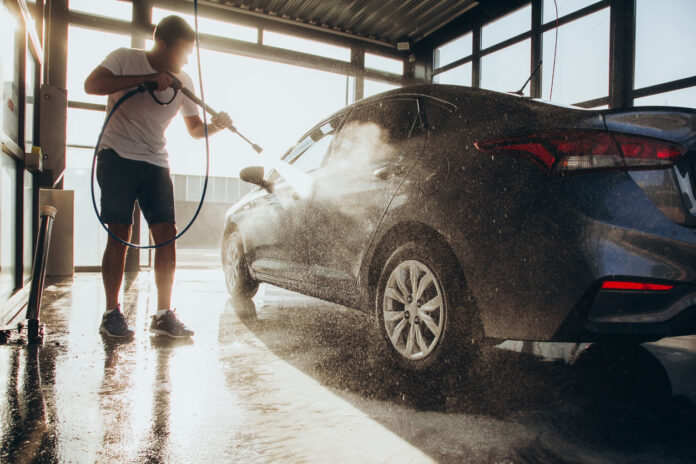 Ein Mann wäscht seinen Wagen mit dem Hochdruckreiniger.