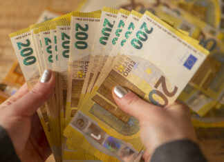 Eine Frau hält viele 200 Euro Scheine in den Händen. Dahinter liegen noch mehr Scheine.