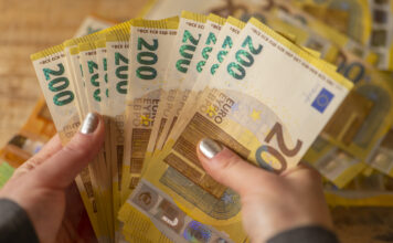 Eine Frau hält viele 200-Euro-Scheine in den Händen. Dahinter liegen noch mehr Scheine.