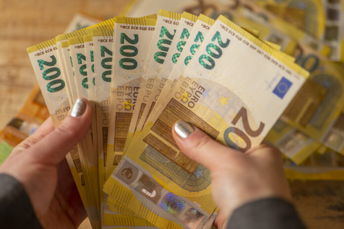Eine Frau hält viele 200-Euro-Scheine in den Händen. Dahinter liegen noch mehr Scheine.