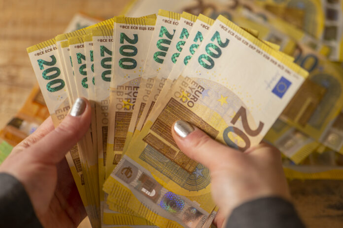 Weibliche Hände mit silbernem Nagellack halten etliche 200-Euro-Scheine zum Zählen. Dahinter liegt noch mehr Geld. Verschwommen erkennt man noch mehr 200-Euro-Scheine sowie einen 50-Euro-Schein.