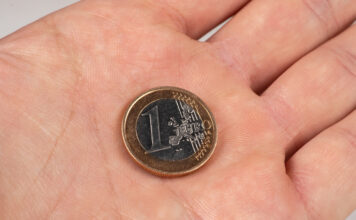 Eine 1-Euro-Münze liegt in der Hand eines Mannes.