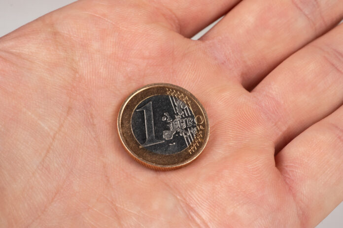 Eine 1-Euro-Münze liegt in der Hand eines Mannes.