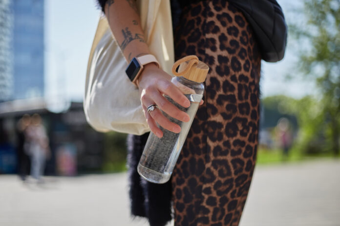Eine junge Frau hält eine Wasserflasche in ihrer Hand und füllt sie dann einer Refill-Station wieder auf.