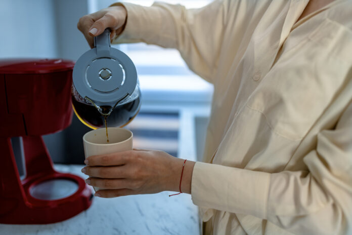 Eine Frau gießt sich Kaffee aus einer Kanne in eine weiße Tasse.