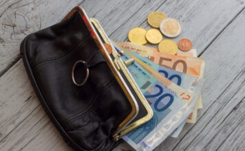 Ein offenes Portemonnaie mit Geldscheinen und Münzen. Die Euros liegen neben dem Geldbeutel.