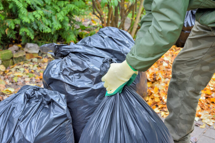 Gartenarbeiter sammelt mit Handschuhen Blätter in schwarzen Plastiktüten