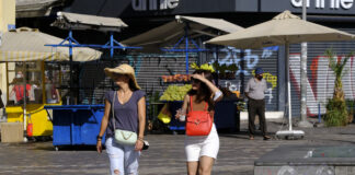 Menschen gehen während einer Hitzewelle durch die Straße in einem Stadtzentrum. Sie tragen ein Cap um sich vor der Sonne zu schützen und Shorts.