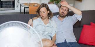 Gestresstes Paar schwitzt vor einem Ventilator