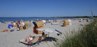 Viele Urlauber entspannen am Sandstrand vor dem Meer auf Decken und in Strandkörben