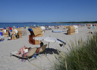 Viele Urlauber entspannen am Sandstrand vor dem Meer auf Decken und in Strandkörben