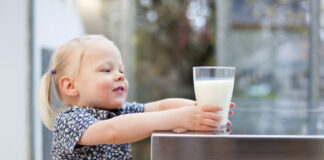 Ein kleines Mädchen greift nach einem Glas Milch.