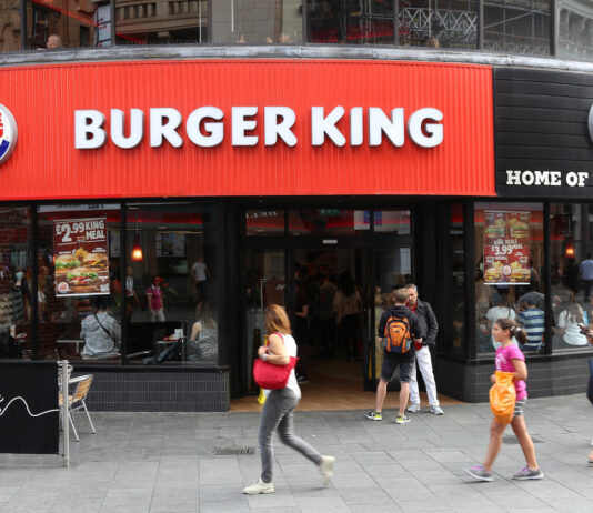 Eine Burger King Filiale an einer Ecke. Davor sammeln sich viele Menschen und drinnen gibt es eine lange Schlange an der Kasse.