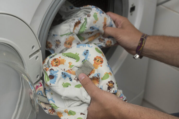 Mann wirft wiederverwendbare Windel in die Waschmaschine.