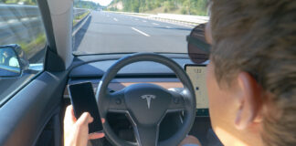 Ein Mann sitzt in einem Tesla und fährt, ohne seine Hände am Lenkrad zu halten.