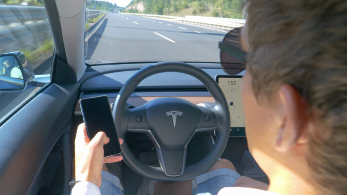 Ein Mann sitzt in einem Tesla und fährt, ohne seine Hände am Lenkrad zu halten.