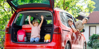 Kinder winken aus einem beladenen Auto.