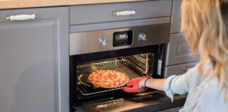 Eine Frau schiebt eine Tiefkühlpizza in den Ofen. Sie hat einen Ofenhandschuh an.