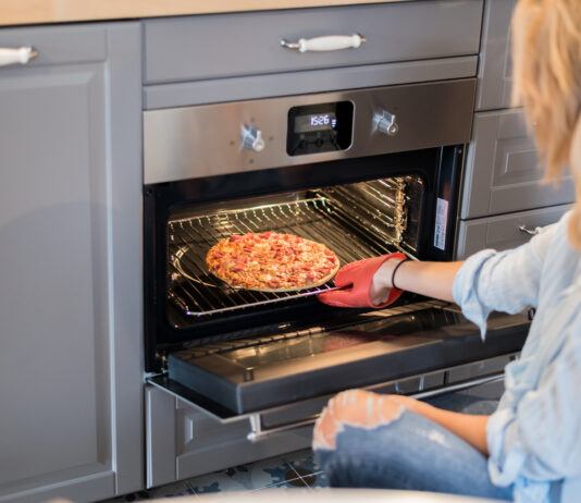 Eine Frau schiebt eine Tiefkühlpizza in den Ofen. Sie hat einen Ofenhandschuh an.