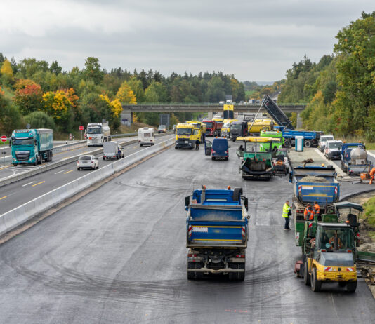 LKW und PKW fahren auf einer Autobahn in beide Richtungen und passieren eine Baustelle. Die Fahrbahn der Bundesstraße oder Autobahn wird erneuert.