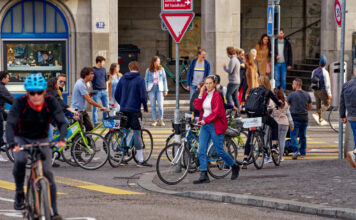 Mehrere Radfahrer überqueren eine Straße zu Fuß, sie schieben ihr Fahrrad.