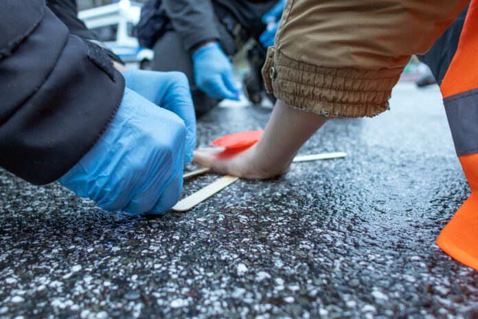 Ein Klima-Aktivist klebt auf der Straße, zwei Hände versuchen ihn zu lösen.