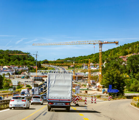LKWs und PKWs sowie andere Fahrzeuge fahren auf einer Autobahn an einer Baustelle vorbei