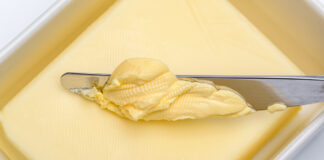 Mit einem Küchenmesser wird Butter aus der Butterdose durch Schmieren entnommen.