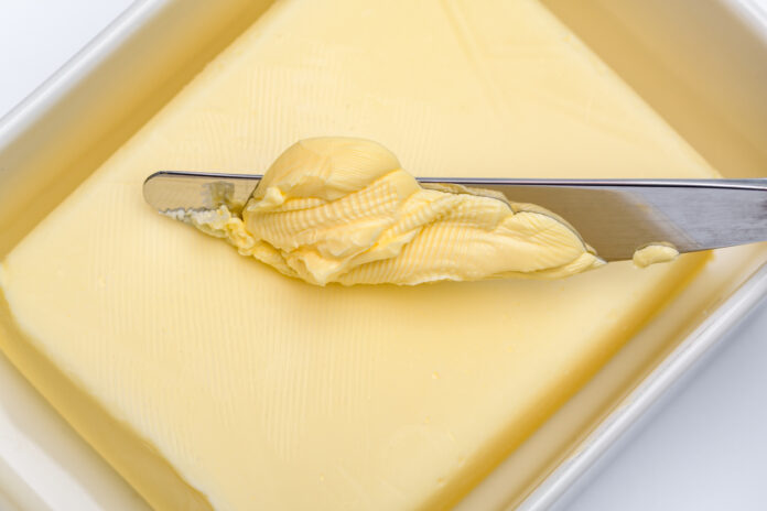 Mit einem Küchenmesser wird Butter aus der Butterdose durch Schmieren entnommen.