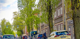Straßenzene mit parkenden Autos, Fahrradweg mit Fahrradfahrern und Straße in einem Wohngebiet Berlins.