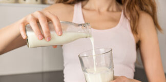 Eine Frau hält ein Glas und gießt sich Milch ein.