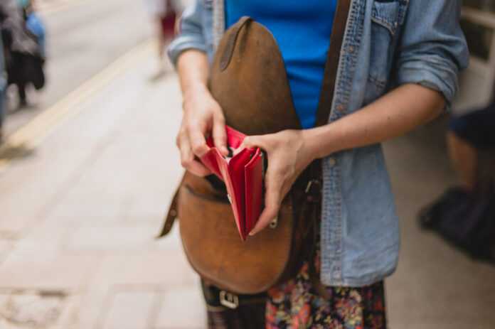 Eine junge Frau öffnet ihren Geldbeutel auf der Straße, um eine Münze herauszuholen