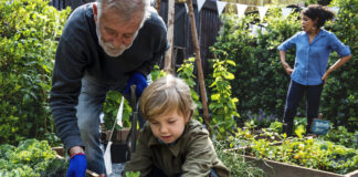 Ein älterer Herr bepflanzt gemeinsam mit der Familie Beete im Garten. Ein Junge und er setzen verschiedene Pflanzen in ein vorbereitetes Beet ein. Sie tragen dabei Handschuhe.