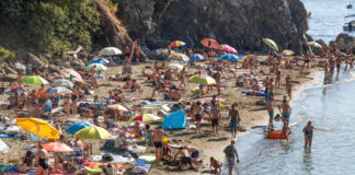 Viele Touristen auf engem Raum am Strand. Es stehen viele Sonnenschirme und die Menschen tragen Badesachen.