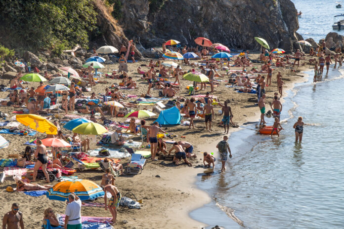Viele Touristen auf engem Raum am Strand. Es stehen viele Sonnenschirme und die Menschen tragen Badesachen.