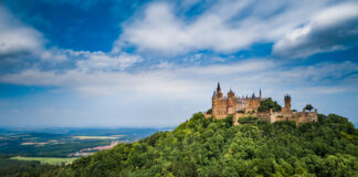Auf einem grünen Berg ist das Schloss Hohenzollern vor blauem Himmel mit Wolken zu sehen.