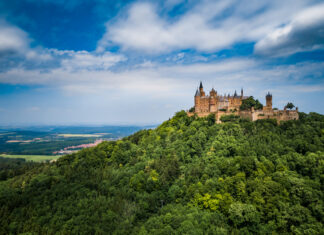 Auf einem grünen Berg ist das Schloss Hohenzollern vor blauem Himmel mit Wolken zu sehen.