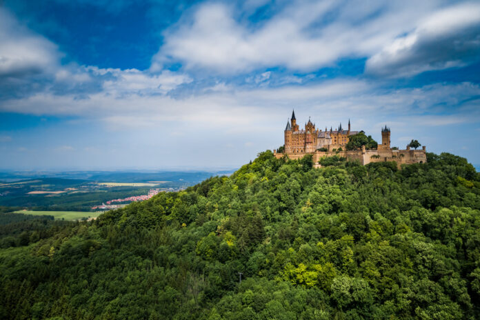Auf einem grünen Berg ist das Schloss Hohenzollern vor blauem Himmel mit Wolken zu sehen.