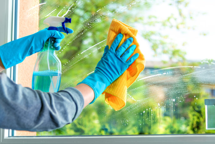 Putzen von Fenstern mit Sprühflasche und Putzlappen