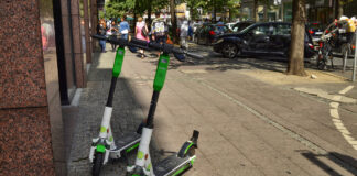 Zwei weiß-grüne E-Scooter parken am Rande einer Einkaufsstraße.