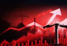 Symbolische Darstellung steigender Energiepreise. Im Vordergrund Stromleitungen und ein Strommast, im Hintergrund ein Schornstein und Hochspannungsleitungen. Darüber Diagrammkurven. Das Bild ist rötlich gefärbt.