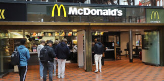 Eine lange Warteschlange vor einem McDonald's- Restaurant. Viele Menschen reihen sich an, teilweise noch vor dem Eingangsbereich, um an der Kasse der McDonald's-Filiale ihre Bestellung für Burger Pommes und Co. aufzugeben.