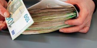 Ein Mann hält einen Geldumschlag mit vielen Geldscheinen darin. Ein 20.000 Euro Zuschuss soll kommen.